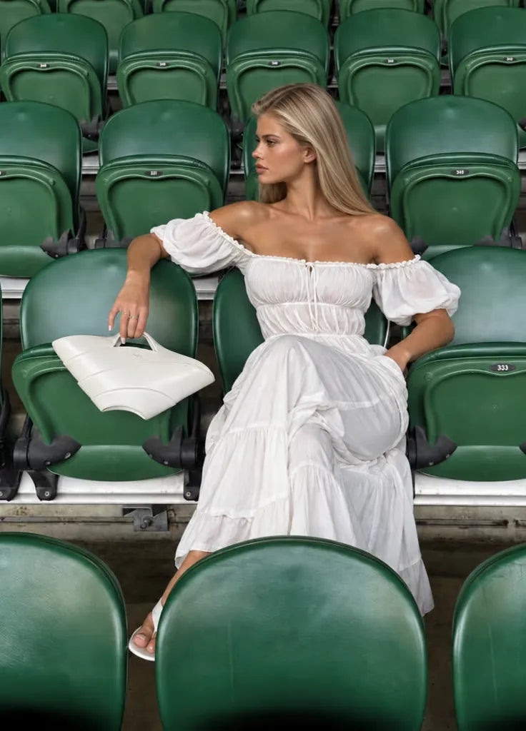 white off-the-shoulder maxi dress worn in green stadium seats